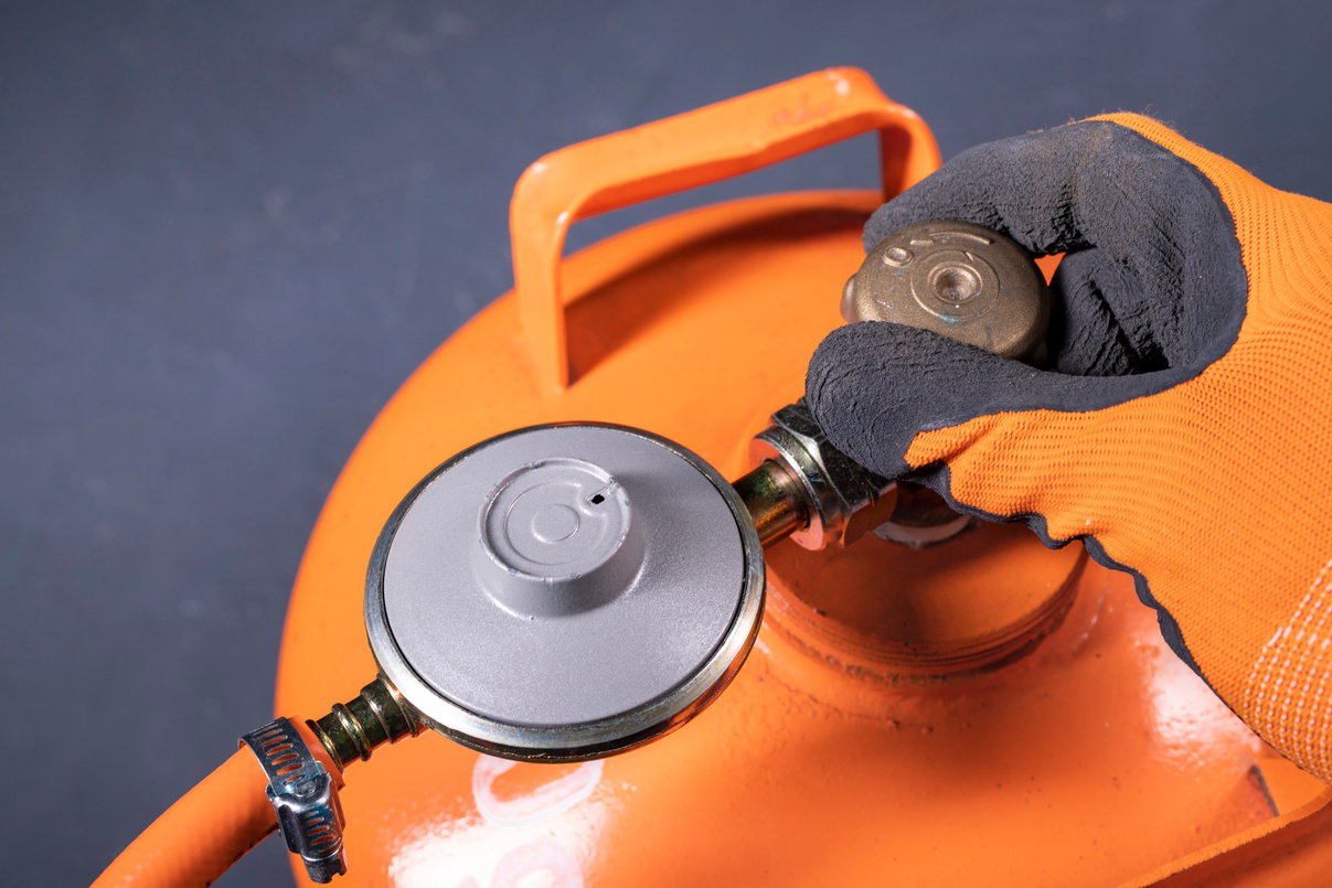 Unscrewing the valve in the propane-butane gas cylinder. Installation work on the gas installation. Dark background.